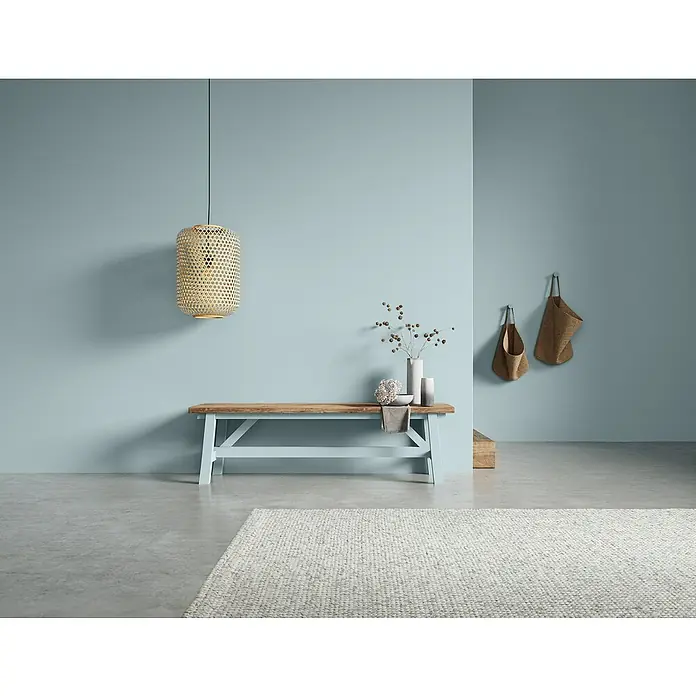 SCHÖNER WOHNEN-Farbe Naturell Wandfarbe Kreidefarbe - Bergseeruhe - helles Blaugrau, Matt, 2,5 l, Konservierungsmittelfrei - Eine moderne Inneneinrichtung mit einer Holzbank, einer gewebten Lampe und dekorativen Elementen an einer blaugrünen Wand.