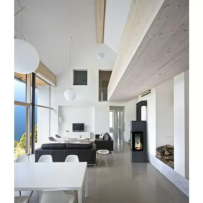 Kratki Kaminofen Thor - 8 kW, Schwarz - Modernes Wohnzimmer mit schwarzen Sofas, weißem Esstisch, Kamin und großen Fenstern mit Seeblick.