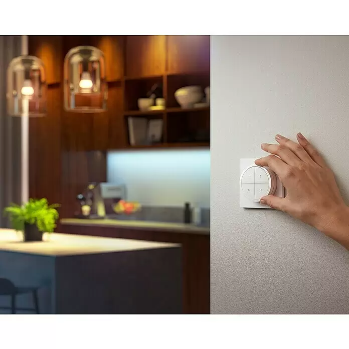 Philips Hue Lichtsteuerung Tap Dialswitch - 6 x 6 x 2 cm, Smart Home-fähig: Ja, Weiß, Dimmbar - Eine Hand stellt einen weißen, runden Smart-Dimmschalter mit vier Tasten ein, der Lichter in einer modernen Küche steuert.