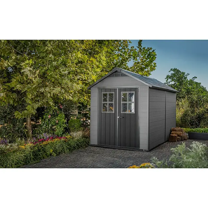Keter Gerätehaus Newton 7511 - Außenmaß inkl. Dachüberstand (B x T): 228 x 350 cm, Kunststoff, Schiefergrau, 7,98 m² - Ein graues Gartenhaus mit Doppeltür und Fenstern, umgeben von üppigem Grün, bietet stilvollen Stauraum im Garten.
