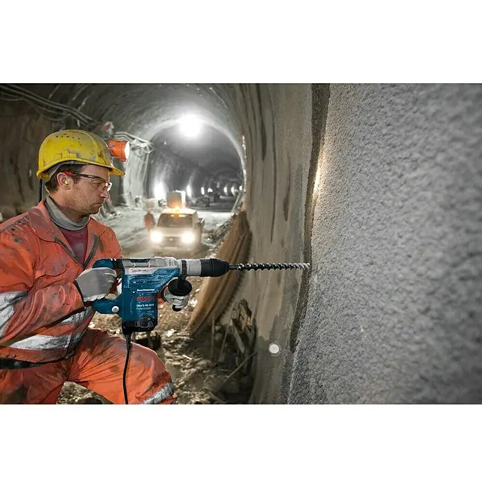 Bosch Professional Martillo perforador GBH 5-40 DCE - 1.150 W, 8,8 J, Alojamiento SDS-MAX - Un trabajador de la construcción utiliza un martillo perforador Bosch en un túnel. El martillo perforador es azul y tiene una broca larga.