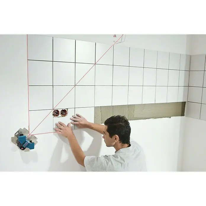 Bosch Professional Fliesenlaser GTL 3 - Max. Arbeitsbereich: 20 m, 4 -tlg. - Ein Handwerker verlegt mit Hilfe eines Laser-Nivelliergeräts weiße Fliesen an einer Badezimmerwand, um ein präzises und professionelles Ergebnis zu gewährleisten.
