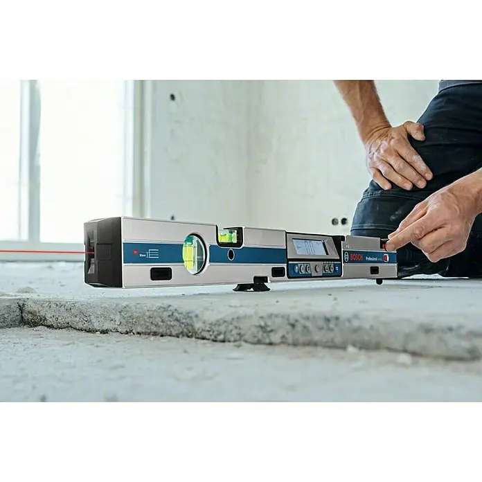 Bosch Professional Digitale Wasserwaage GIM 60 L - Länge: 61,8 cm - Der Bosch Professional GIM 60 Digitalneigungsmesser wird von einer Person auf einer Betonfläche bedient. Das Gerät projiziert einen roten Laser.