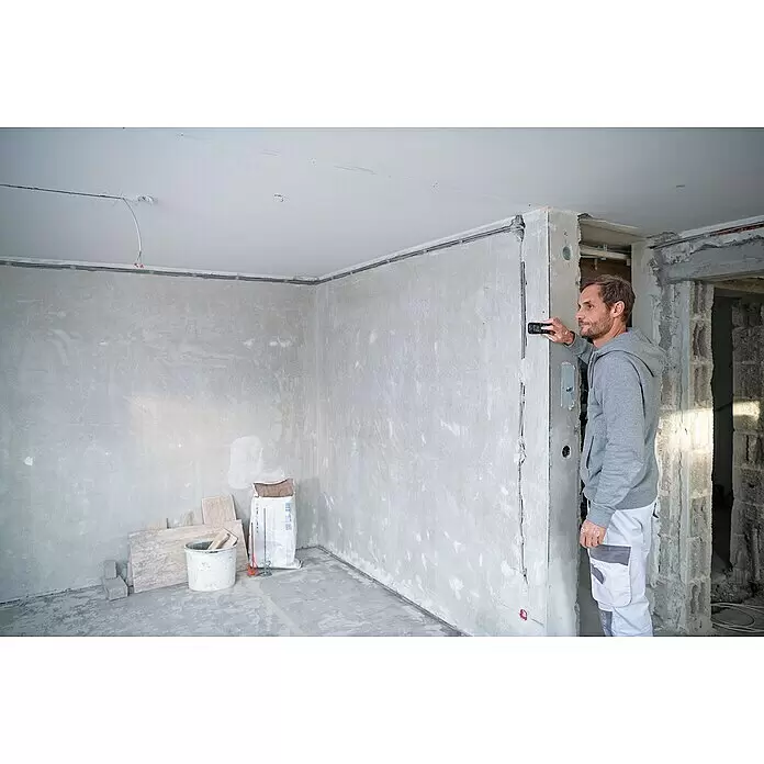Bosch Professional Laserentfernungsmesser GLM 50-27 CG - Anzahl Akkus: 1 Akku, Messbereich: 0,05 - 50 m - Mann misst mit schwarzem und orangefarbenem Laser-Entfernungsmesser eine graue Wand in einem Raum im Bau.