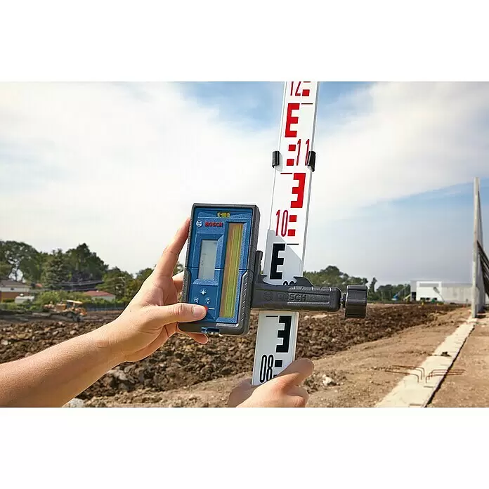 Bosch Professional Laserempfänger LR 45 - Passend für: GRL 300 HV, GRL 300 HVG, GRL 400 H Professional - Hände halten einen blau-schwarzen Bosch Laserempfänger an einer weißen Nivellierlatte auf einer Baustelle.