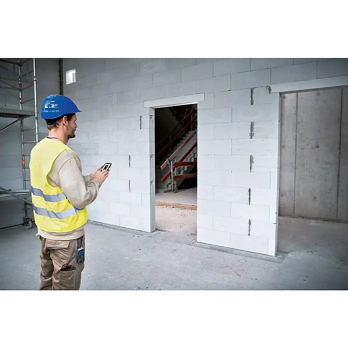 Bosch Professional Laserentfernungsmesser GLM 50-27 CG - Anzahl Akkus: 1 Akku, Messbereich: 0,05 - 50 m - Bauarbeiter mit blauer Helm und gelber Warnweste macht Fotos mit dem Handy in einem unfertigen Gebäude mit einer Treppe im Hintergrund.
