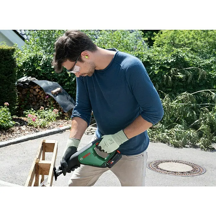 Bosch Power for All 18V Akku-Säbelsäge AdvancedRecip 18 - 18 V, 1 Akku, 2 Ah, Leerlaufhubzahl: 0 /min - 3.100 /min - Der Mann benutzt eine Bosch Akku-Universalsäge, um ein Holzstück zu sägen, wobei er Schutzbrille und Handschuhe trägt.