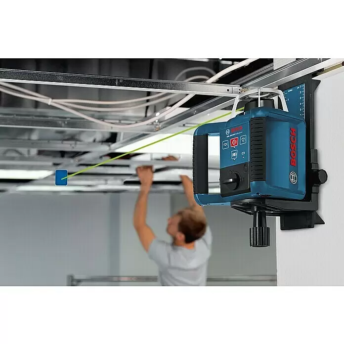 Bosch Professional Rotationslaser GRL 300 HV - Arbeitsbereich: Ø 60 m (ohne Empfänger), 11 -tlg. - Blaues Bosch-Laser-Nivelliergerät an der Wand montiert, das eine grüne Laserlinie für die Deckenjustierung durch einen Arbeiter aussendet.