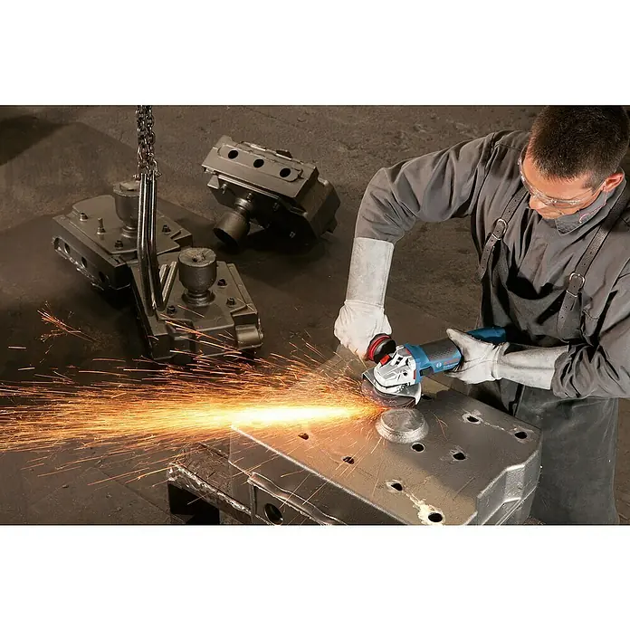 Bosch Professional Elektro-Winkelschleifer GWS 17-125 - 1.700 W, Durchmesser Scheibe: 125 mm, Leerlaufdrehzahl: 11.500 U/min - Ein Arbeiter benutzt einen Bosch Winkelschleifer mit Schutzbrille, Handschuhen und Schürze zum Schleifen eines Metallstücks, wodurch Funken entstehen.