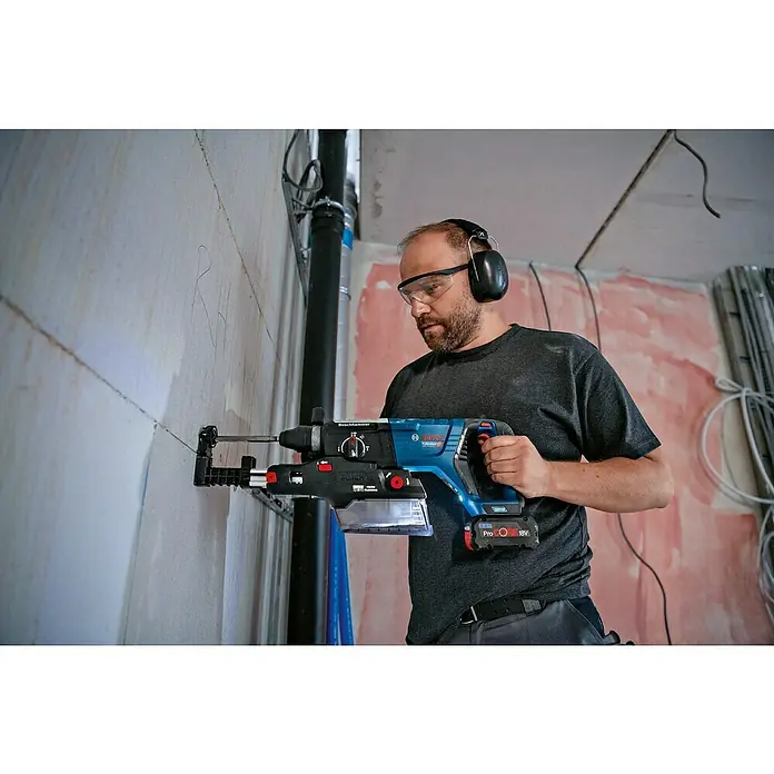 Bosch Professional Staubabsaugung GDE 28 D - Passend für: Bosch Professional Akku-Bohrhammer GBH 18V-28 DC - Ein Bauarbeiter mit Schutzbrille und Kopfhörern bedient einen Bosch Bohrhammer mit Staubabsaugung an einer Wand.