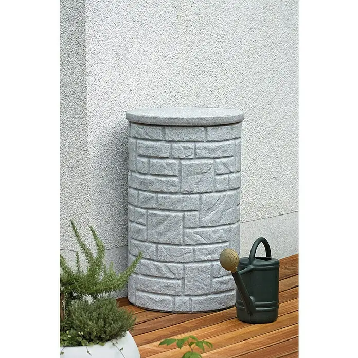 Arves Regenspeicher Arcado - 230 l, Granitfarben - Dekorativer, grauer Regenwassertank in Steinoptik neben einer grünen Gießkanne auf einer Holzterrasse vor einer weißen Wand.