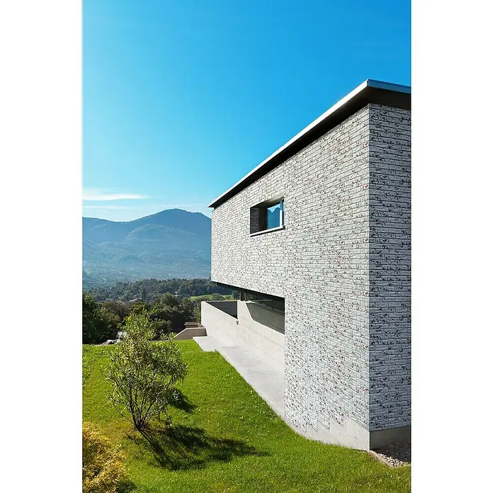 Stegu Verblendstein-Ecke Country 680 - 20,5 cm x 9,5 cm x 14 mm, Hellgrau, Steinoptik - Ansicht eines modernen zweistöckigen Backsteingebäudes mit einer Rasenfläche im Vordergrund und Bergen im Hintergrund.