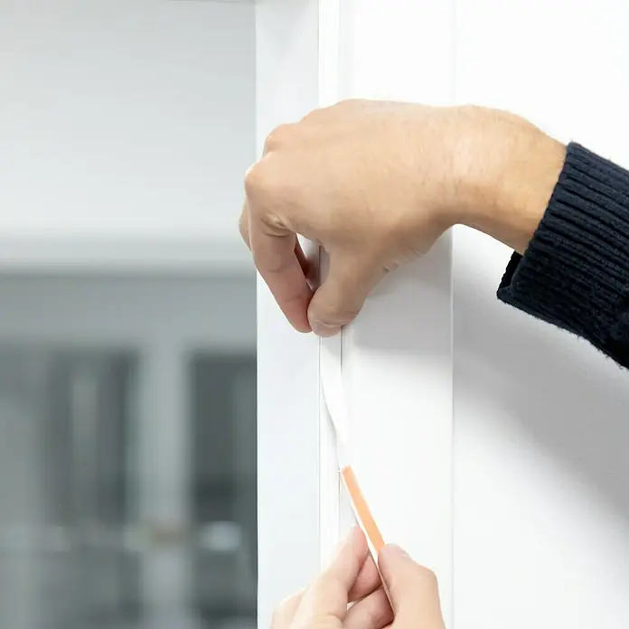 Primo Universaldichtung Densa 25 - Weiß, 6 m, Passend für: Fenster, Türen, Möbel mit Spaltenbreite 2 – 5 mm - Ein Mann befestigt selbstklebende Dichtungsband an einem weißen Türrahmen, um Zugluft zu verhindern.