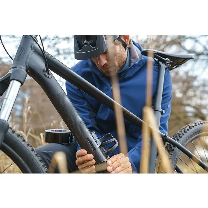 Tesa Ultra Power Reparaturgewebeband Extreme - Schwarz, 10 m x 50 mm - Nahaufnahme eines Fahrrads, das von einer Person mit schwarzem Klebeband repariert wird.