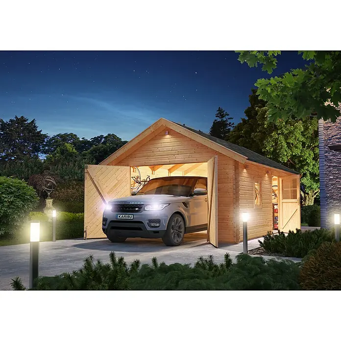 Karibu Garage - Holz, 19,4 m², Wandstärke: 40 mm, Satteldach - Dieses Bild zeigt eine Karibu-Garage mit einem geparkten Auto davor, beleuchtet von Außenleuchten in einer nächtlichen Gartenszene.