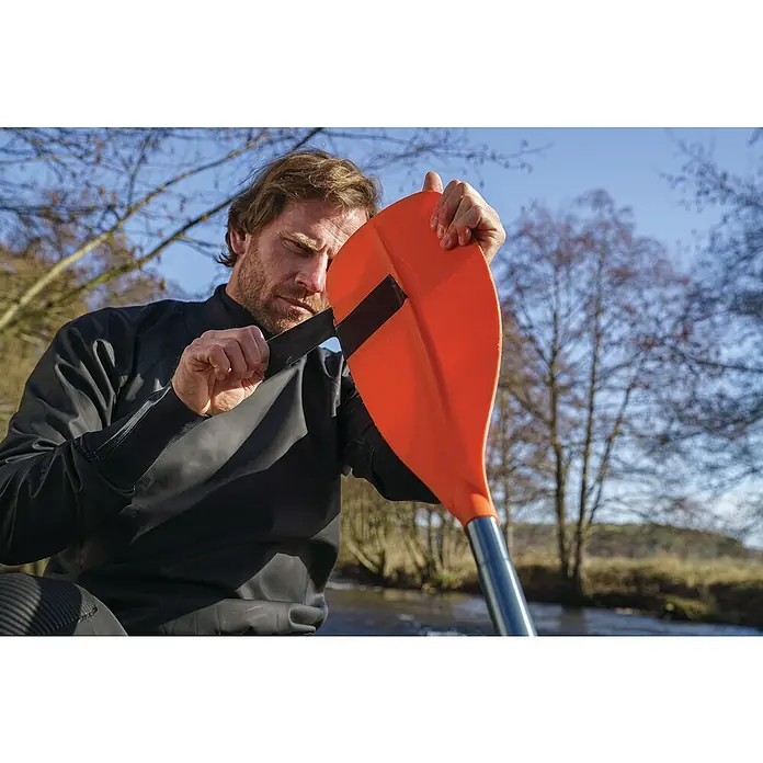 Tesa Ultra Power Unterwasser-Klebeband Under Water - Schwarz, 1,5 m x 50 mm - Mann, der ein orangefarbenes Paddel mit einem schwarzen Griff in der Hand hält, vor einem Hintergrund aus Bäumen und Fluss.