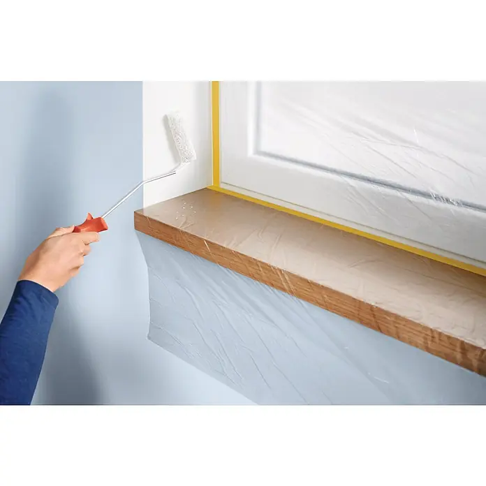 Tesa Abdeckfolie Easy Cover Perfect+ - L x B: 17 m x 260 cm - Nahaufnahme eines Wandanstrichs mit einer Farbwalze. Der Fensterbereich ist mit Folie und gelbem Klebeband geschützt.