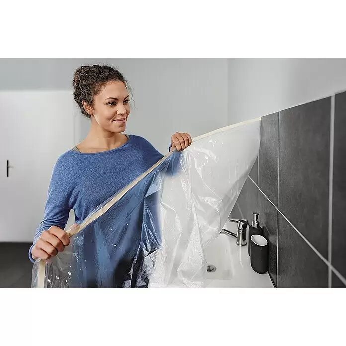 Tesa Abdeckfolie Easy Cover Economy - L x B: 17 m x 260 cm - Frau bringt transparente Abdeckfolie mit Klebeband an, um Waschbecken und Fliesenwand bei Renovierung zu schützen.