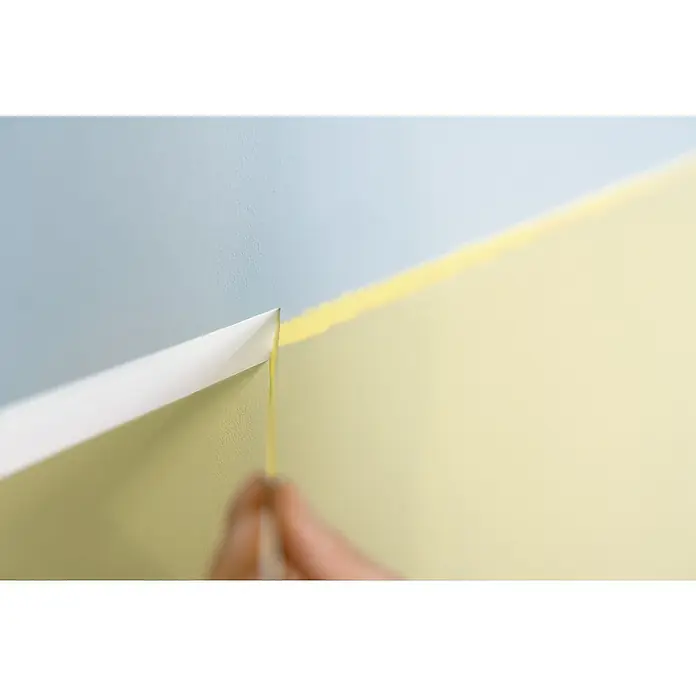 Tesa Malerband Professional - 50 m x 30 mm - Ein detailreiches Bild zeigt das vorsichtige Entfernen von Malerkreppband von einer frisch gestrichenen Wand, wobei die präzise Linie zwischen den Farben hervorgehoben wird.