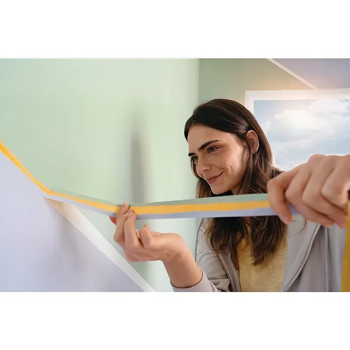 Tesa Malerband Perfect+ - 50 m x 30 mm - Frau klebt farbiges Klebeband an die Wand, um ein geometrisches Muster zu erstellen. DIY-Dekoration für ein modernes Zuhause.