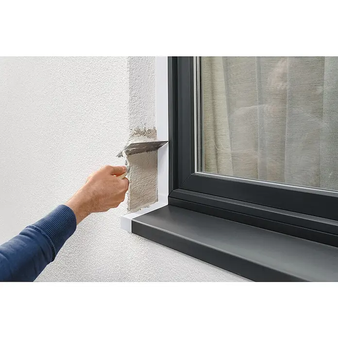 Tesa Putzband PE - Weiß, L x B: 33 m x 5 cm, Von Hand einreißbar - Ein Mann glättet Putz an einer Wand neben einem Fenster mit einem Spachtel, um eine saubere Oberfläche zu schaffen.