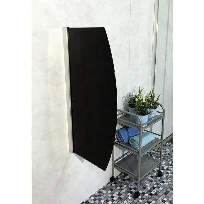 GEO Urinal-Trennwand Radius 10 - 50 x 90 cm, Glas, Schwarz - Wandmontierter Klapptisch in Schwarz mit silbernem Rahmen, daneben ein Rollwagen mit Handtüchern und Pflanzen.