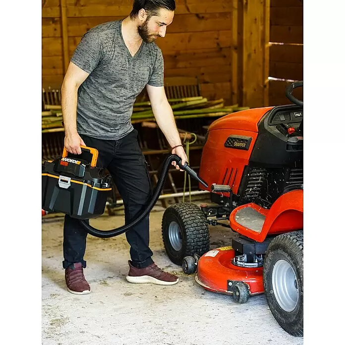 Worx PowerShare 20V Akku-Nass-Trockensauger WX031.9 - 20 V, Ohne Akku, Behältervolumen: 8 l - Mann reinigt einen roten Aufsitzrasenmäher mit einem schwarz-orangen Worx-Handstaubsauger.