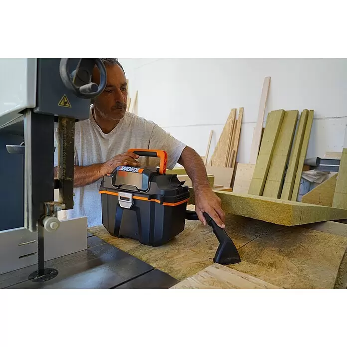 Worx PowerShare 20V Akku-Nass-Trockensauger WX031.9 - 20 V, Ohne Akku, Behältervolumen: 8 l - Ein Mann nutzt einen schwarz-orangen WORX Werkstattsauger, um Holzspäne in einer Werkstatt zu reinigen.
