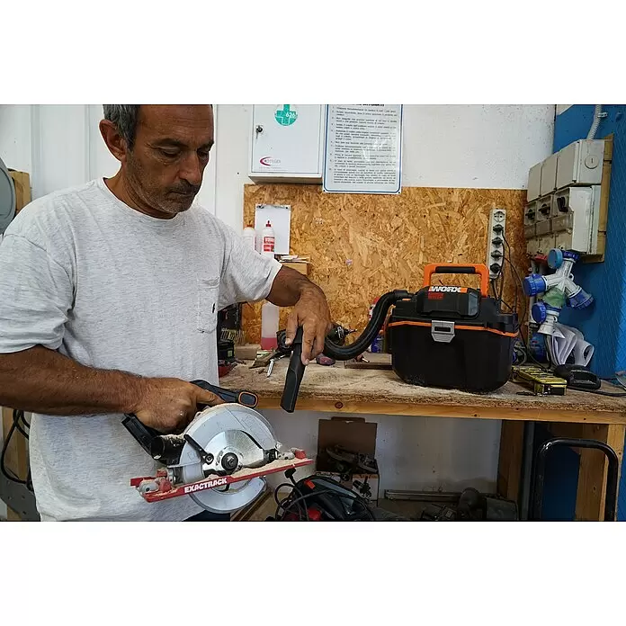 Worx PowerShare 20V Akku-Nass-Trockensauger WX031.9 - 20 V, Ohne Akku, Behältervolumen: 8 l - Mann nutzt schwarzen und orangefarbenen WORX Werkstattsauger zur Sägemehlaufnahme beim Betreiben einer EXACTRACK Kreissäge.