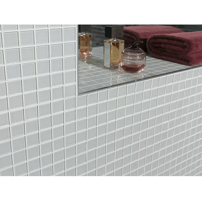 Mosaikfliese Quadrat Crystal Uni CM 4040 - 32,7 x 30,2 cm, Weiß, Glänzend - Detailaufnahme von weißen Mosaikfliesen an einer Badezimmerwand mit Ablagefläche, auf der Handtücher und Parfümflaschen stehen.