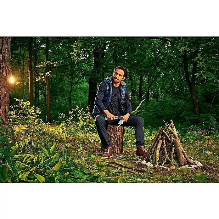 Cellfast Universalaxt U600 Ergo - Länge: 26 cm - Mann sitzt auf einem Baumstamm, hält eine blau-graue Axt neben einem Holzhaufen, bereit für ein Lagerfeuer.