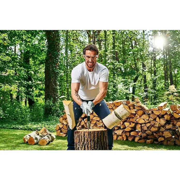 Cellfast Universalaxt U600 Ergo - Länge: 26 cm - Ein Mann spaltet Holz mit einer Axt. Holzscheite liegen bereit für den Kamin. Er trägt Schutzkleidung für mehr Sicherheit.