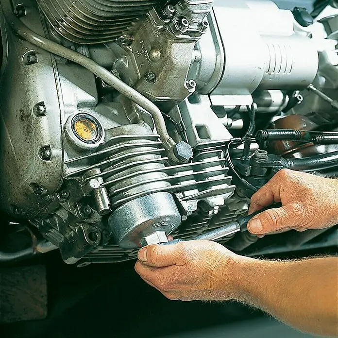 Hazet Universal-Ölfilter-Schlüssel 2169 - Schlüsselweite: 74,4 mm, Antriebsgröße: ⅜″ Vierkant - Ein Mechaniker, der einen Ölfilter an einem Motor mit einem Schraubenschlüssel festzieht, der für Wartungsarbeiten verwendet wird.