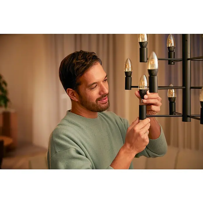 Philips Hue Smart-LED-Lampen Set Smart Vintage E27 - E14, Dimmbar, Warmweiß, 300 lm, 4,5 W, 2 Stk. - Ein Mann schraubt eine Philips Hue Kerzenlampe in einen schwarzen Lampenhalter. Die Lampe ist Teil einer dekorativen Leuchte.