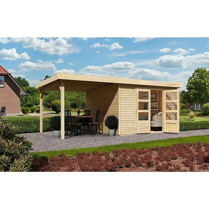 Karibu Gartenhaus Askola - Außenmaß inkl. Dachüberstand (B x T): 558 x 331 cm, Holz, Natur, Mit Anbaudach - Ein helles Holzgartenhaus mit Carport, Terrassenmöbeln und Pflanzen auf einer gepflasterten Fläche unter blauem Himmel mit Wolken.