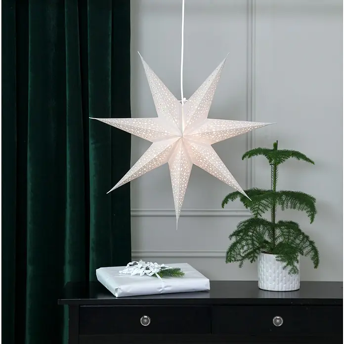Eglo Estrella LED Blinka - 60 cm, Blanco - Una pantalla de lámpara de estrella de papel blanca cuelga sobre una mesa con un regalo y una planta en maceta, creando un ambiente festivo.
