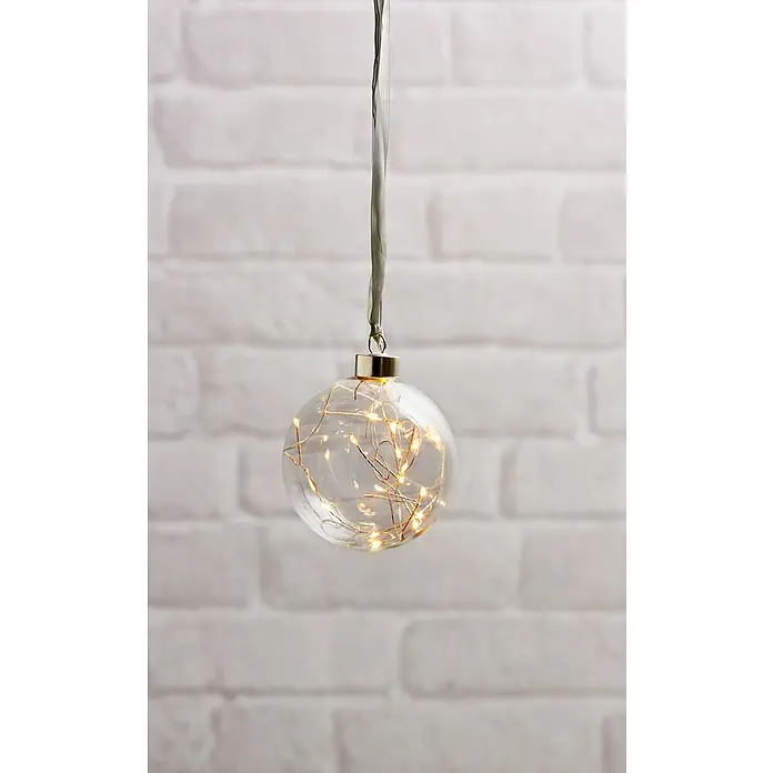 Eglo Lámpara colgante LED redonda Glow - 0,18 W, Diámetro: 10 cm, Blanco cálido, Gris - Una esfera decorativa llena de luz cuelga de una cinta gris, mostrando luces blancas cálidas sobre una pared de ladrillos blanca.