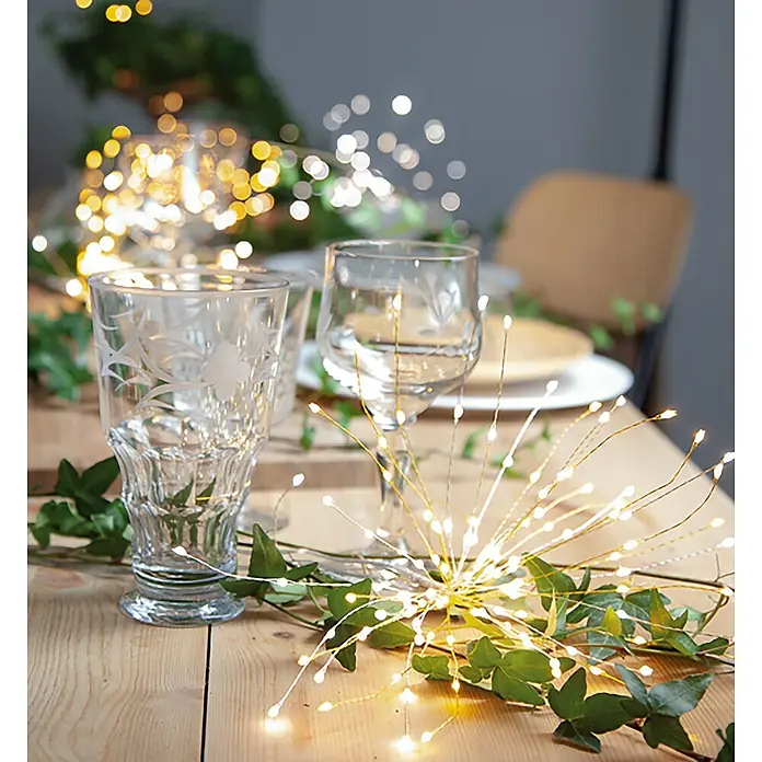 Eglo Lámpara colgante LED redonda Destellos - 3,6 W, Ø x Al: 26 x 26 cm, Blanco frío, Número de bombillas: 60 ud. - Mesa festiva con copas elegantes, vegetación y luces starburst que brillan cálidamente, creando un ambiente acogedor.