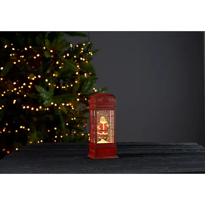 Eglo Figura LED navideña Cabina - 8,5 x 8,5 x 22 cm, Rojo, LED - Decoración navideña con una bola de nieve en forma de cabina telefónica con una figura de Papá Noel sobre una mesa frente a un árbol de Navidad.