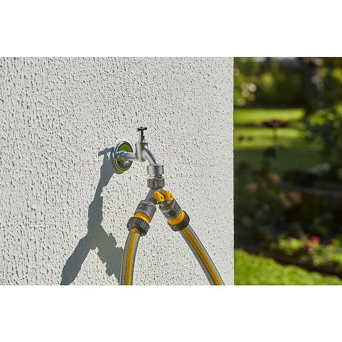 Neptun 2-Wege-Ventil - Gewindegröße Wasserhahn: 33,3 mm (1″), 26,5 mm (¾″), 21 mm (½″) - Ein Wasserhahn mit einem gelb-grauen Gartenschlauchanschluss an einer weißen Wand. Perfekt für die Gartenbewässerung!