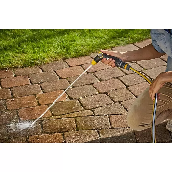 Neptun Brause - Kunststoff - Eine Person sprüht mit einer gelb-schwarzen Gartenschlauchdüse Wasser auf einen gepflasterten Weg.