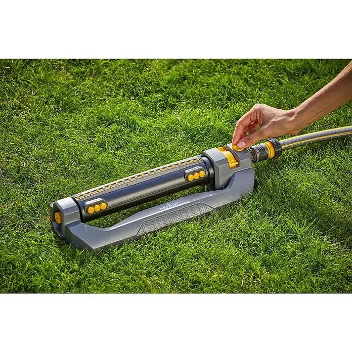 Neptun Viereckregner - Max. Regnerfläche: 460 m² - Eine Person bedient einen oszillierenden Rasensprenger von Neptun auf einem grünen Rasen, um den Garten zu bewässern.