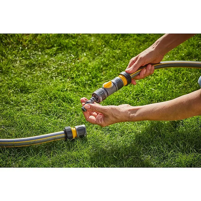 Neptun Schlauchkupplung - ¾″, Ohne Wasserstopp - Gartenschlauch mit praktischem Anschlussstück wird auf einer grünen Wiese verbunden, ideal für die Gartenbewässerung.