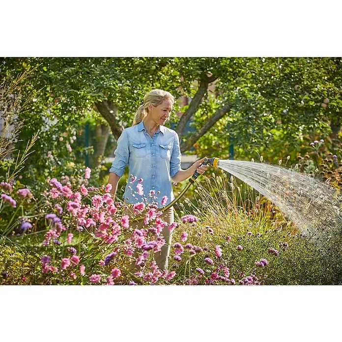 Neptun Bewässerungsbrause - Anzahl Sprühformen: 7 Stk. - Eine Frau gießt mit einem gelben Wasserschlauch Blumen in einem üppigen Garten, wobei der Fokus auf dem Bewässerungssystem liegt.