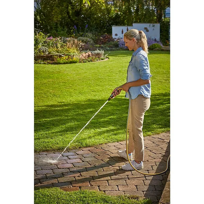 Neptun Reinigungsspritze - Kunststoff - Eine Frau reinigt einen Steinweg mit einem gelben Hochdruckreiniger. Das Gerät beseitigt Schmutz und Algen effektiv.