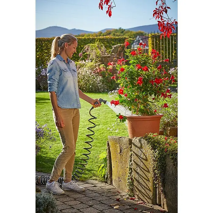 Neptun Spiralschlauch-Set - Länge: 15 m, Kunststoff - Frau gießt eine Mandevilla-Pflanze mit einem Gartenschlauch. Der Flexi-Schlauch ermöglicht eine bequeme Bewässerung von Topfpflanzen.