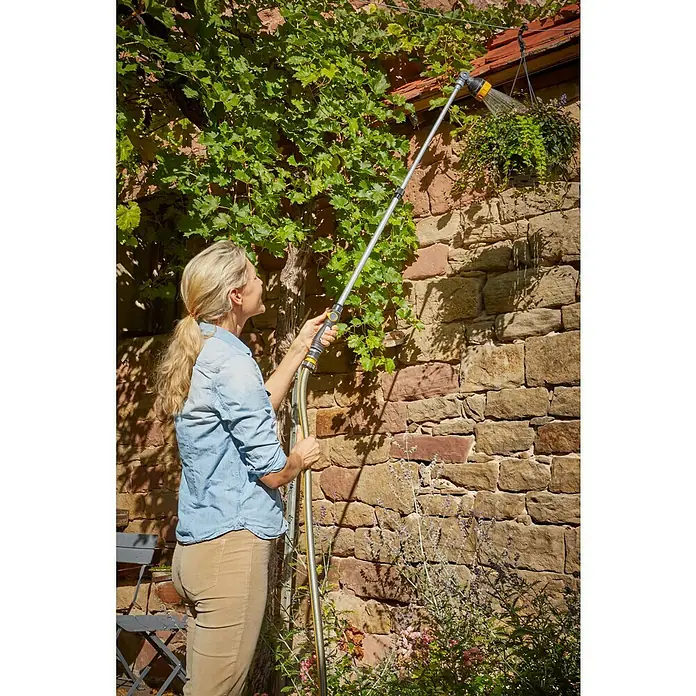 Neptun Teleskop-Gießstab - Länge: 84 cm, Aluminium/Kunststoff - Frau gießt mit einer GARDENA Gartendusche Pflanzen an einer Mauer, die mit Wein bewachsen ist. Das Bewässerungssystem ist effizient und präzise.