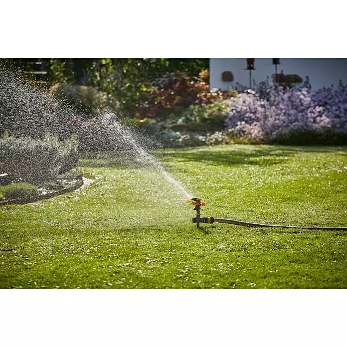 Neptun Kreisregner - Kunststoff, Max. Regnerfläche: 410 m² - Ein orange-schwarzer Rasensprenger bewässert einen grünen Rasen, Wassertropfen sind im Sonnenlicht sichtbar.