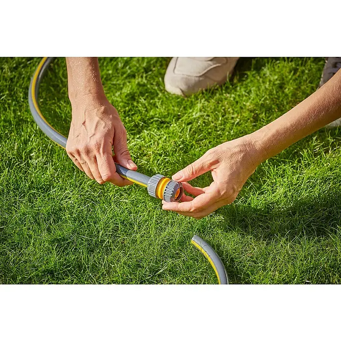 Neptun Universal-Reparaturstück - ½″ - Eine Person befestigt einen gelb-grauen Gartenschlauch mit einem grauen und gelben Anschlussstück auf einer Rasenfläche.