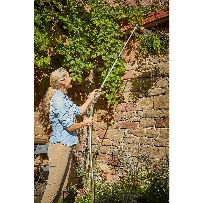 Neptun Teleskop-Gießstab - Länge: 84 cm, Aluminium/Kunststoff - Eine Frau bewässert mit einem GARDENA Bewässerungsaufsatz Blumen in einem hängenden Topf an einer Steinmauer. Bewässerungsgeräte für Pflanzen.